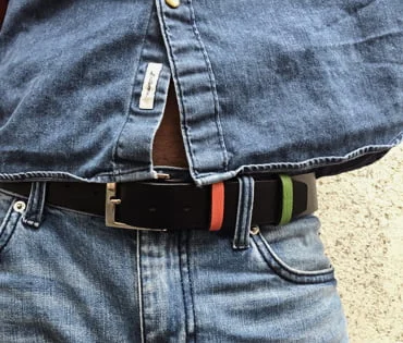 Personne portant une chemise en jean bleu et un jean, avec une ceinture en cuir noir avec des bandes rouges et vertes.