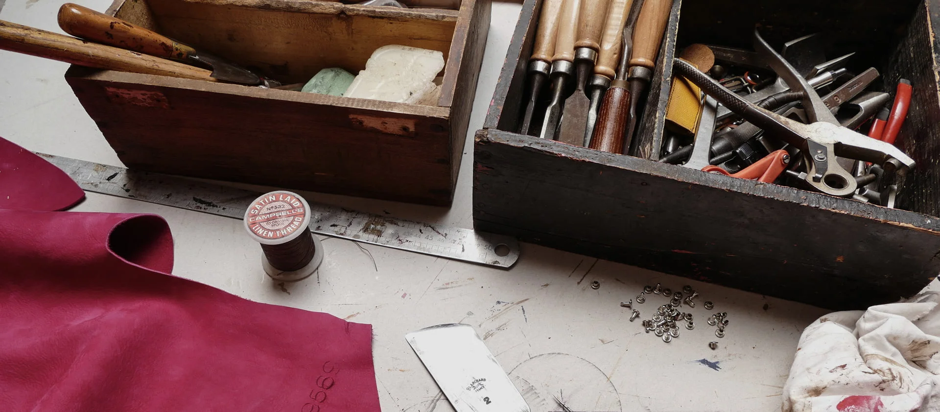 Un espace de travail avec du cuir, du fil, des outils de couture, une règle et deux boîtes en bois.