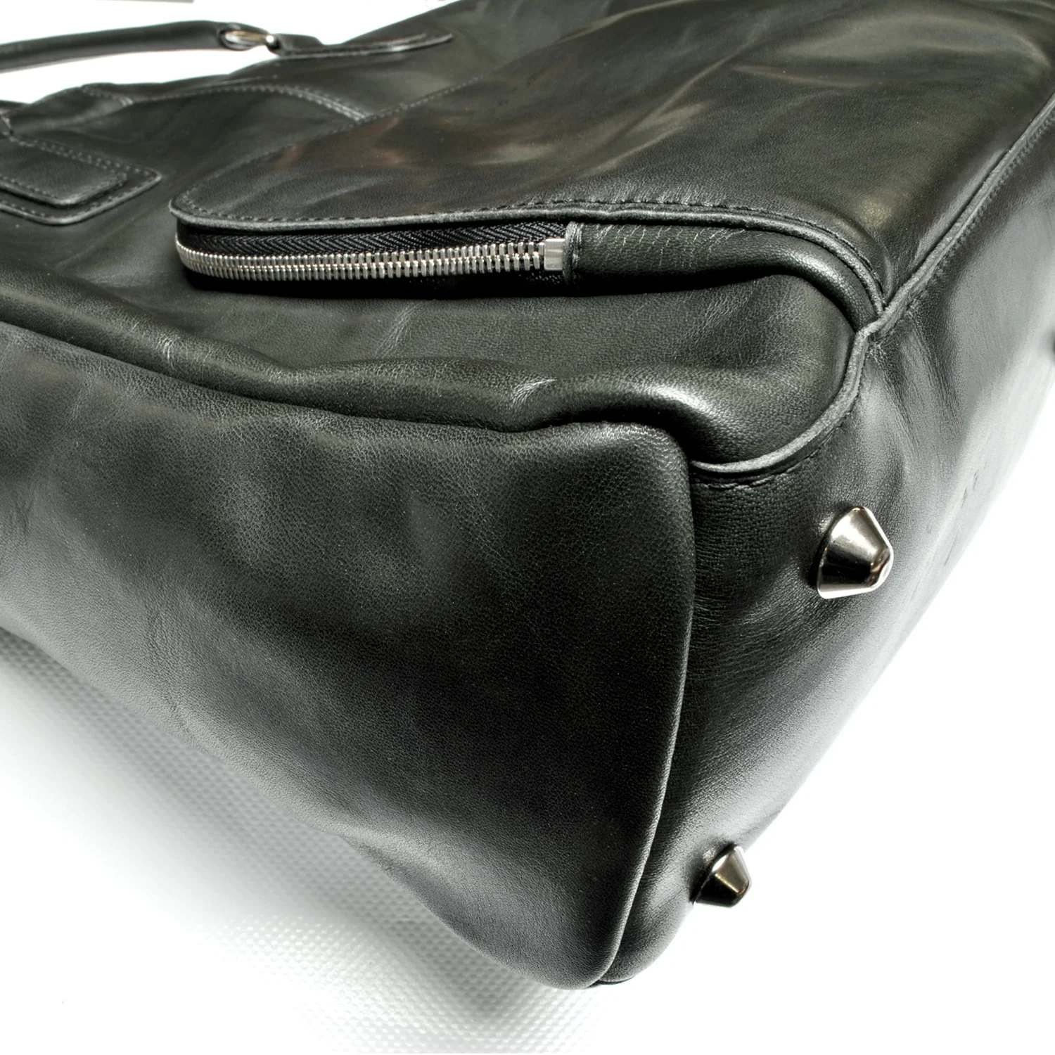 Gros plan d'un sac en cuir noir avec des clous métalliques à la base et une fermeture éclair visible sur un côté.