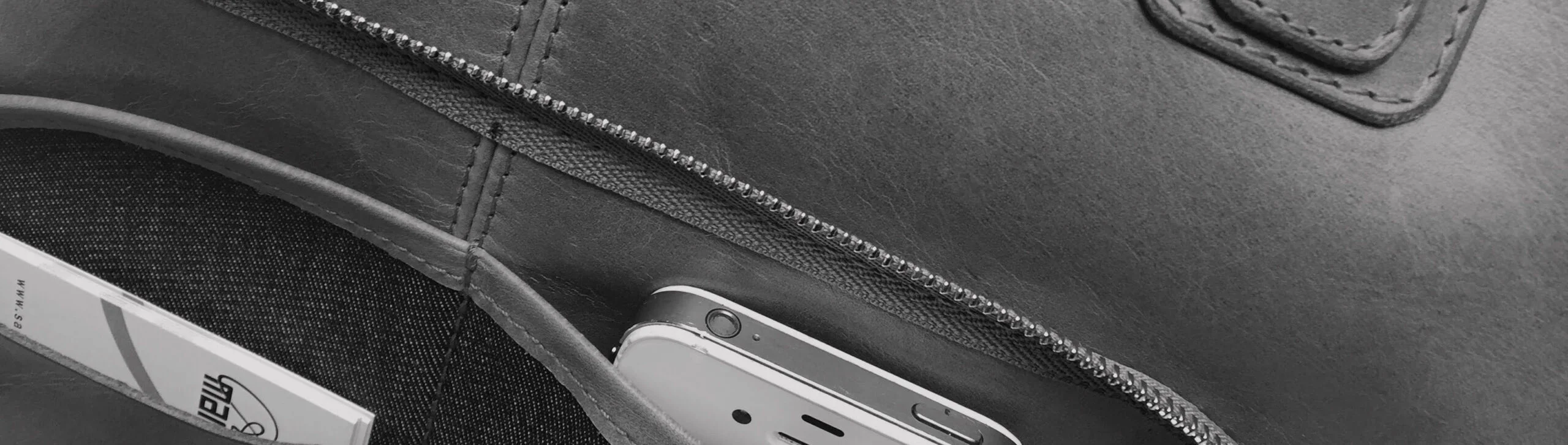 Gros plan d'une poche de sac en cuir ouverte avec un téléphone visible et quelques cartes à l'intérieur.