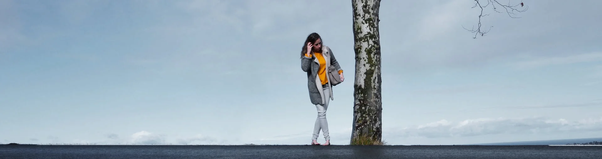 Une personne se tient près d’un arbre, avec un ciel couvert en arrière-plan.