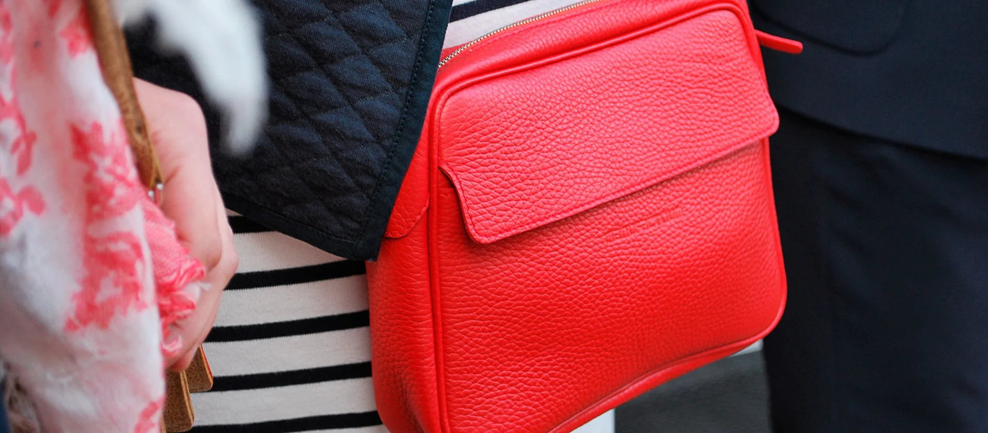 Gros plan d'une personne portant un sac à main texturé rouge attaché sur son corps, debout à côté de personnes portant des vêtements à motifs.