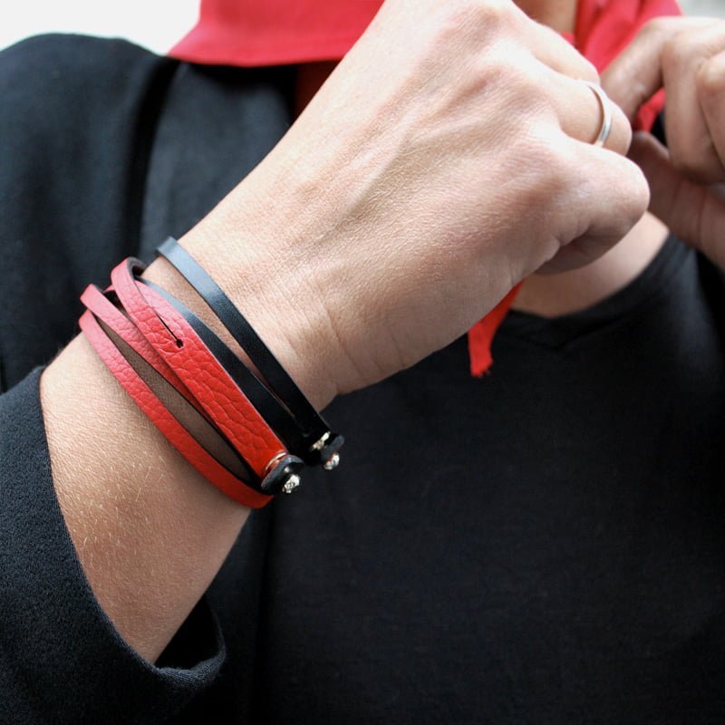 Une personne portant une chemise noire ajuste un foulard rouge. Le poignet est orné de bracelets en cuir noir et rouge.
