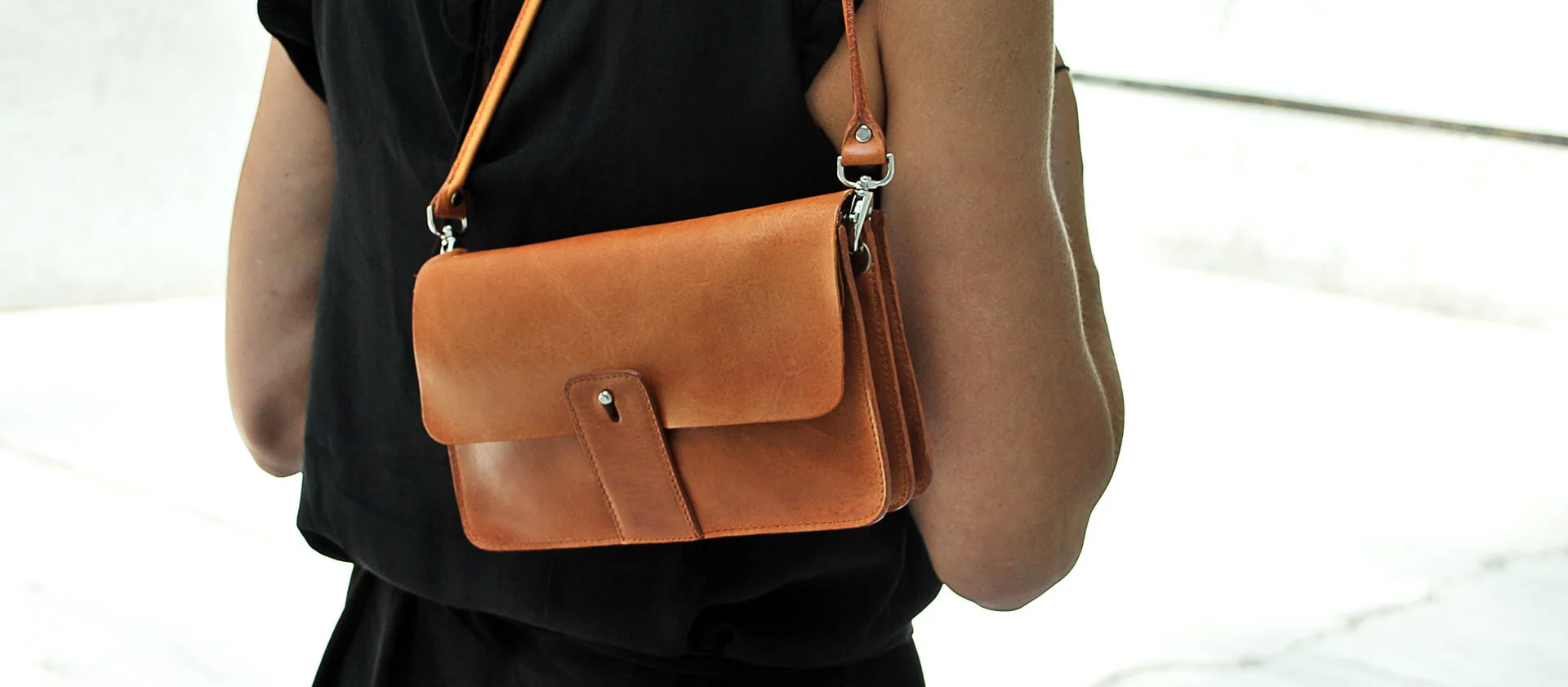Personne portant une tenue noire avec un sac à bandoulière en cuir marron sur l'épaule, regardant ailleurs.