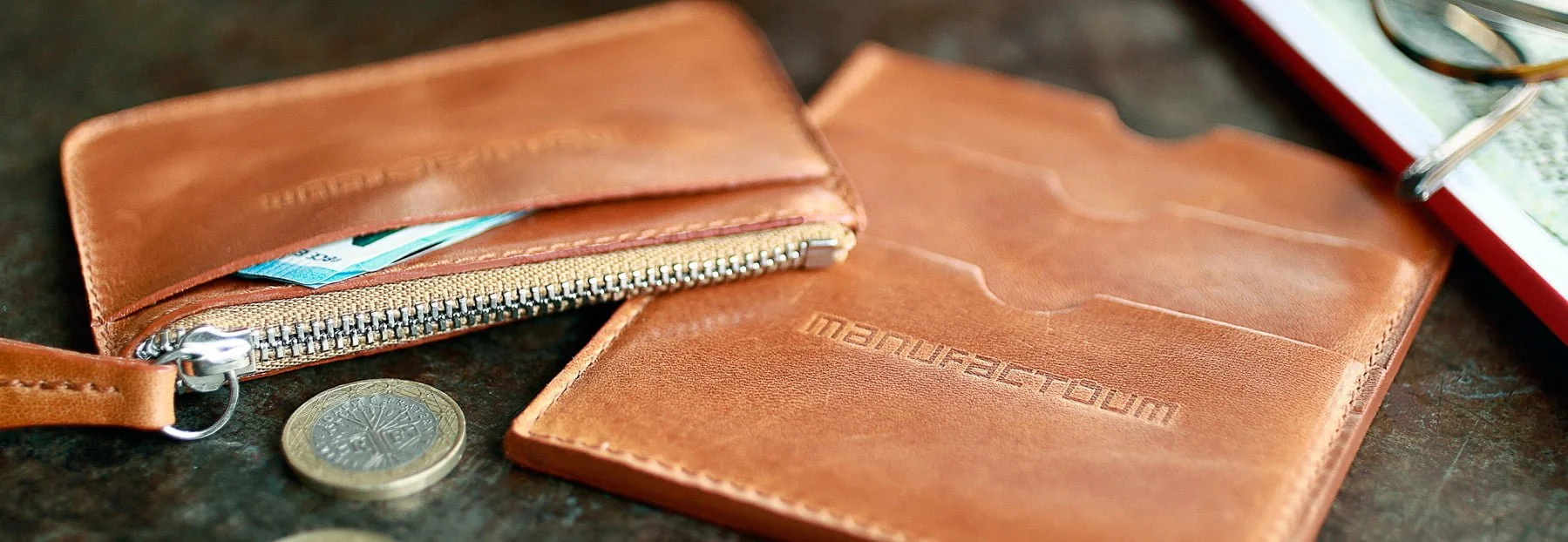 Portefeuille et porte-cartes en cuir marron sur une table avec quelques pièces à proximité.