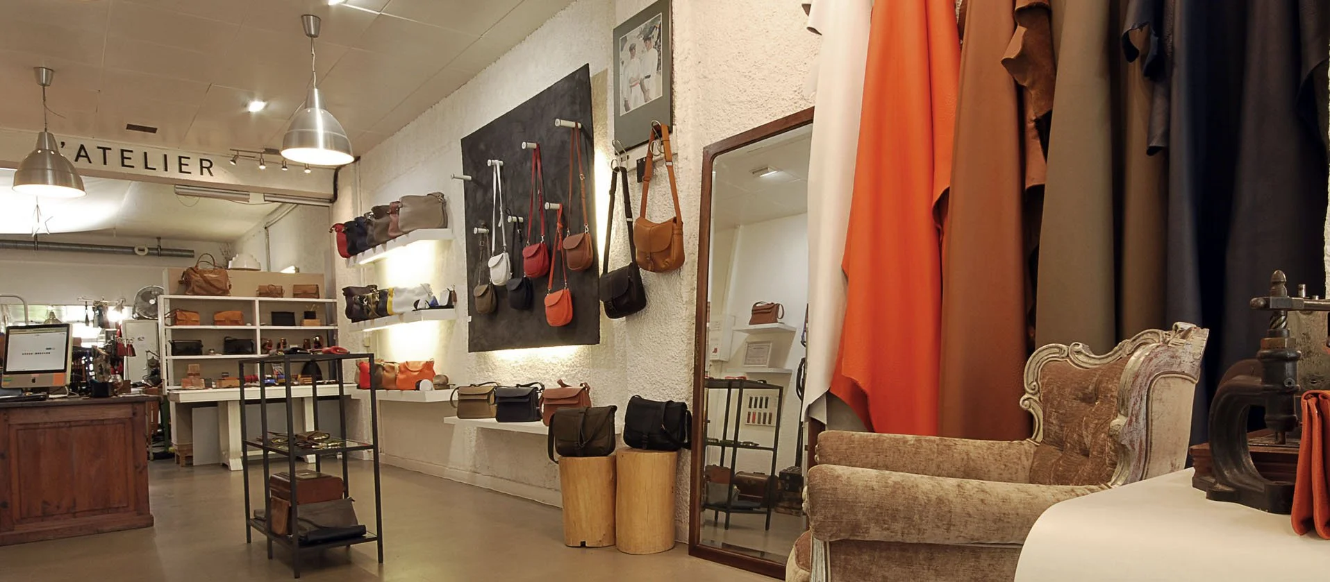Une boutique présentant des sacs à main et des rouleaux de tissu, avec un décor aux tons neutres, un fauteuil vintage et des présentoirs d'accessoires sur des étagères et des supports.