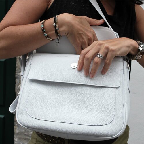 Personne fouillant dans un sac à main en cuir blanc, portant plusieurs bracelets et une bague.