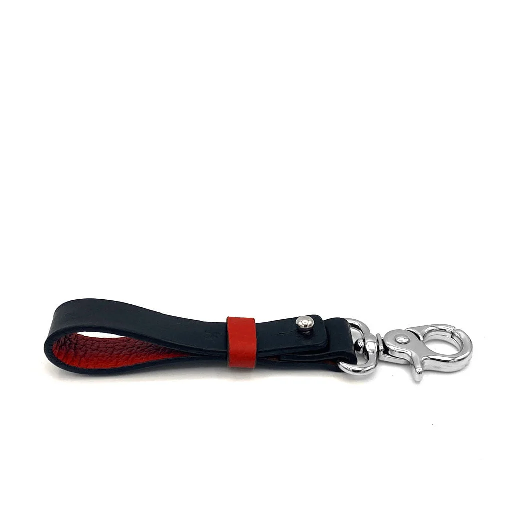 Un porte-clés en cuir noir et rouge avec un fermoir en métal argenté sur fond blanc.