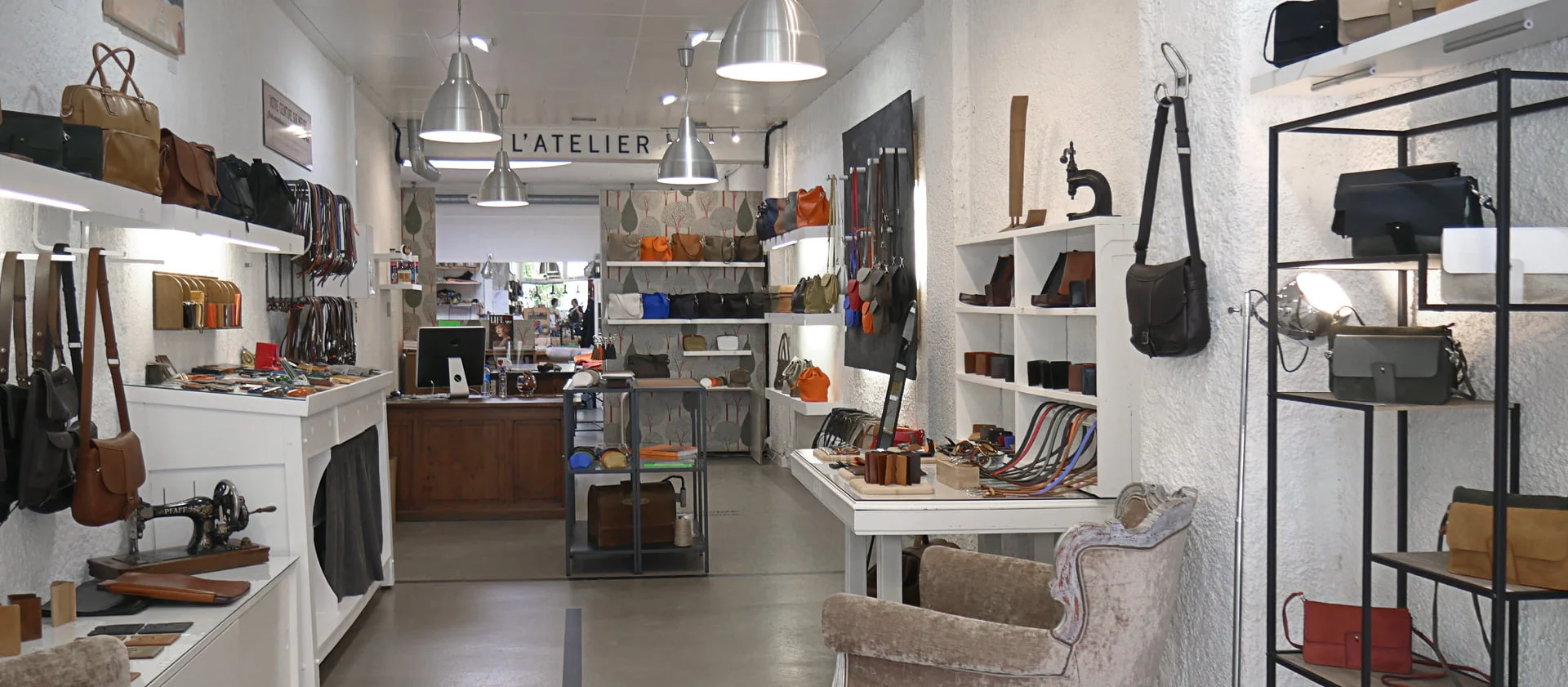 Un magasin de maroquinerie bien éclairé avec des sacs, des portefeuilles et des accessoires exposés sur des étagères et des tables. Un comptoir est visible en arrière-plan.