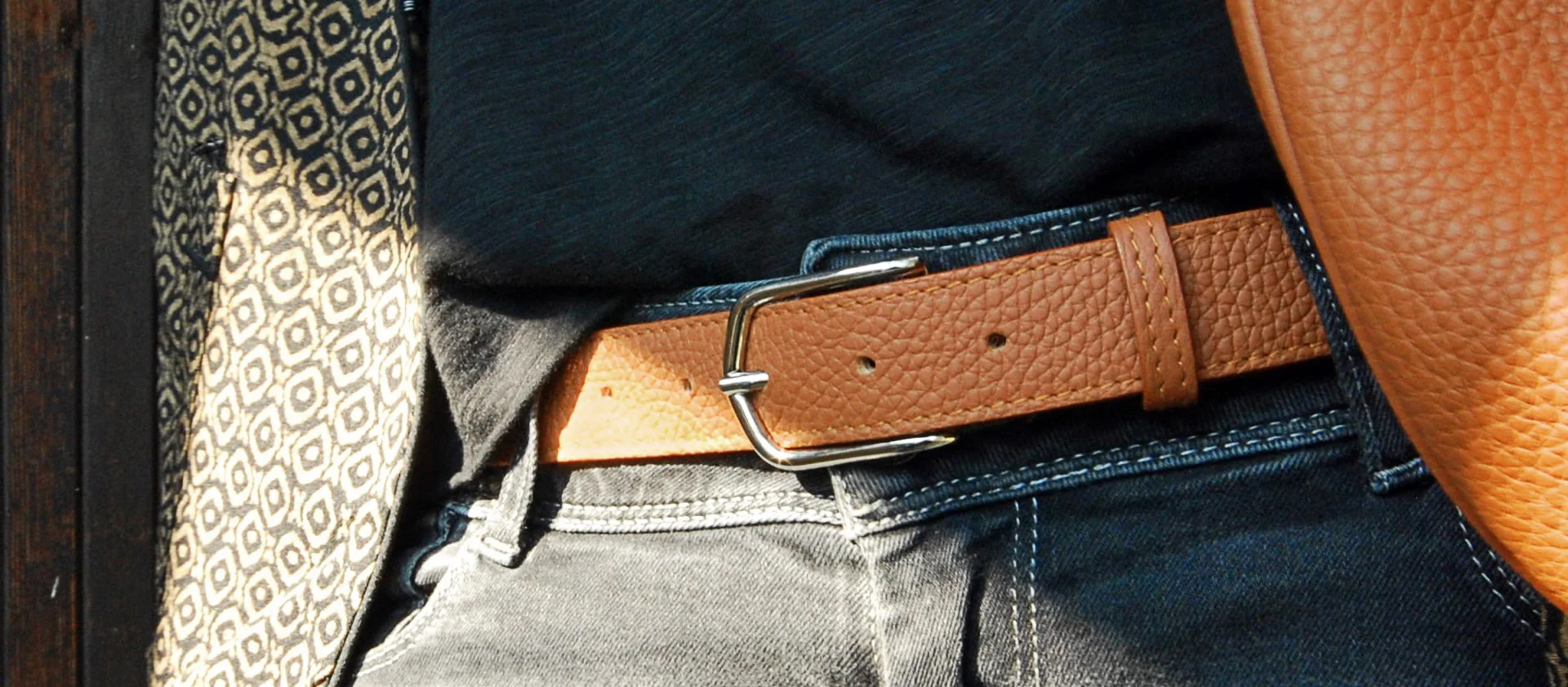 Une ceinture en cuir marron avec une boucle argentée est attachée autour d'un jean bleu.