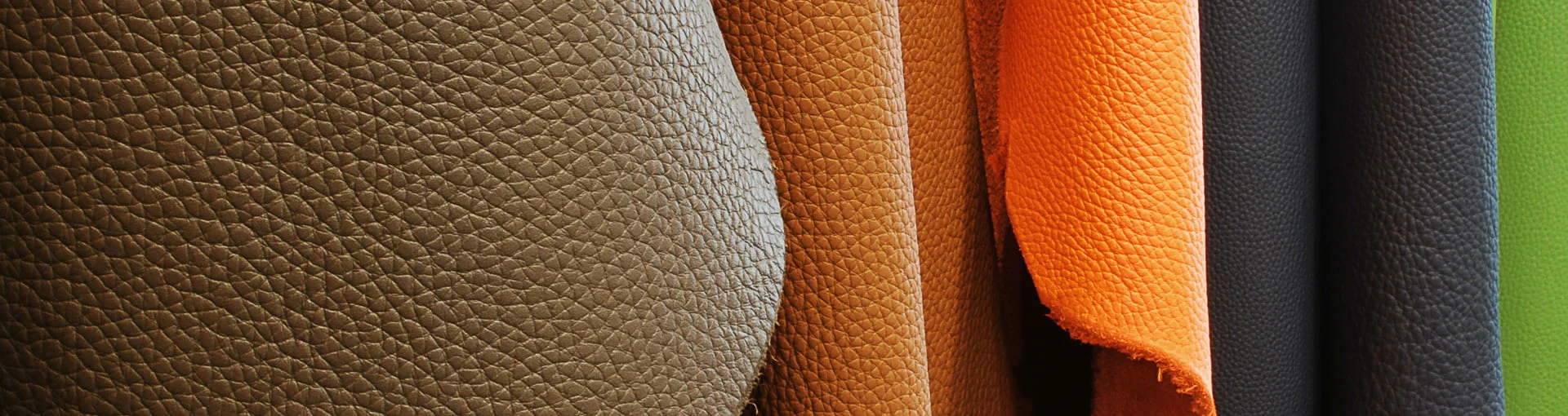 Gros plan d'échantillons de cuir texturé de différentes couleurs, dont le marron, le beige, l'orange, le noir et le vert, suspendus verticalement en rangée.