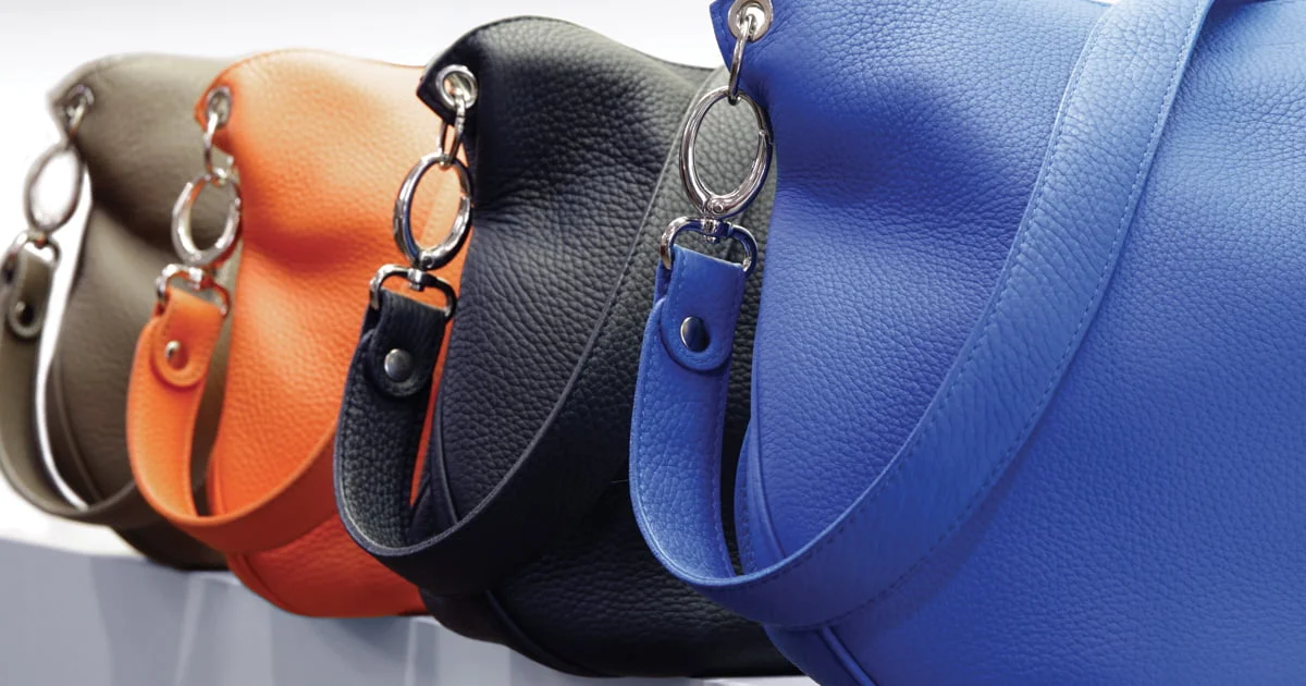 Quatre sacs à main en cuir vert olive, orange, noir et bleu sont présentés en rangée, chacun comportant un anneau et un fermoir en argent.