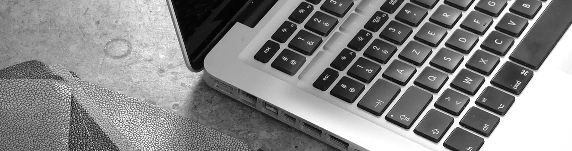 Image en noir et blanc d'un ordinateur portable ouvert avec un clavier AZERTY, placé sur une surface texturée à côté d'un ordinateur portable fermé.