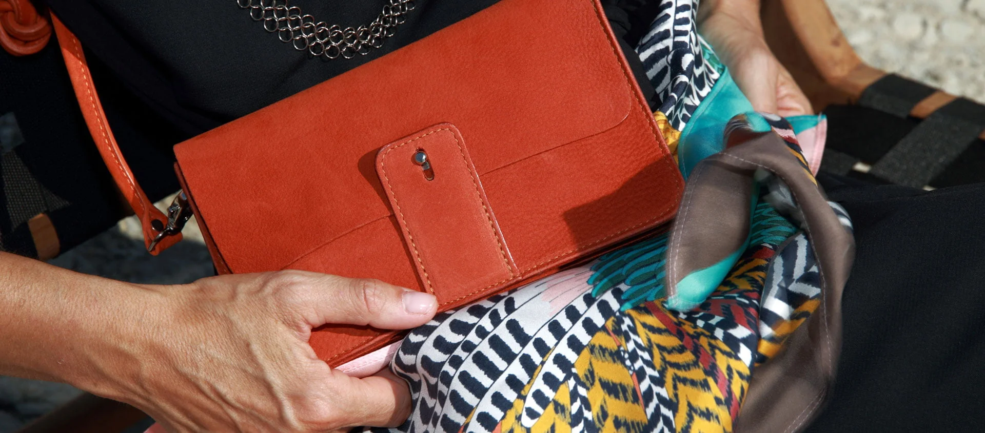 Une personne tient une pochette en cuir orange et une écharpe à motifs colorés tout en étant assise.