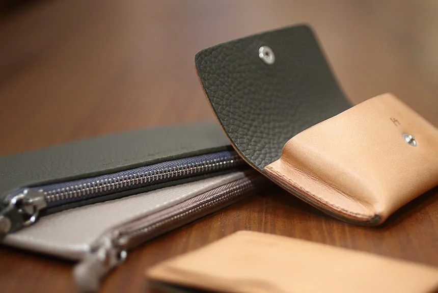 Gros plan de deux portefeuilles en cuir sur une surface en bois, l'un ouvert montrant son intérieur, l'autre fermé par une fermeture éclair visible.