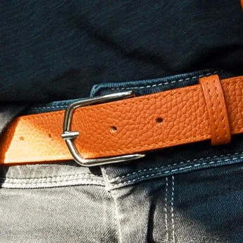 Gros plan d'une ceinture en cuir orange avec une boucle argentée, portée avec un jean bleu et une chemise noire.