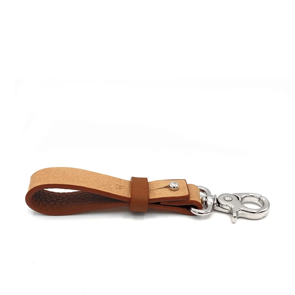 Un porte-clés en cuir marron avec un design en boucle et un fermoir en métal argenté se trouve sur un fond blanc.