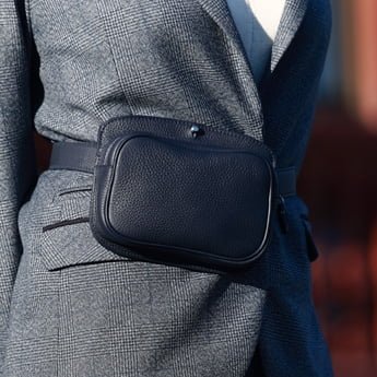 Personne portant un blazer à carreaux gris avec un sac ceinture en cuir noir attaché autour de la taille.