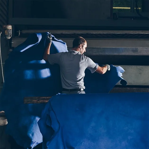 Une personne dans un atelier manipule un grand morceau de tissu bleu, l'ajustant soigneusement sous une machine.