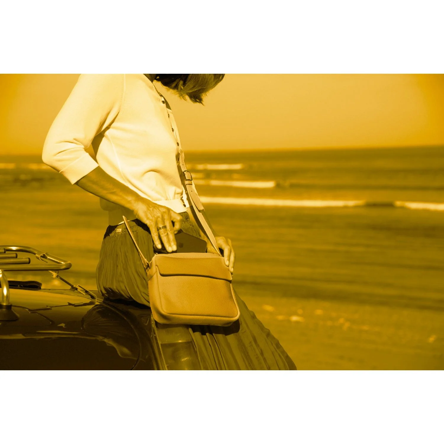 Une personne place la ZOE dans un sac tout en s'appuyant sur une voiture près de la plage, avec l'océan en arrière-plan. L'image présente une teinte jaune.