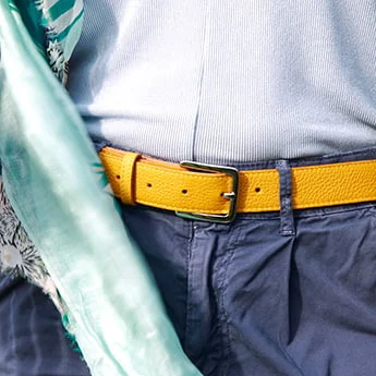 Une personne porte une ceinture jaune avec un pantalon bleu et une chemise bleu clair. Un foulard à motifs est drapé sur l'épaule.
