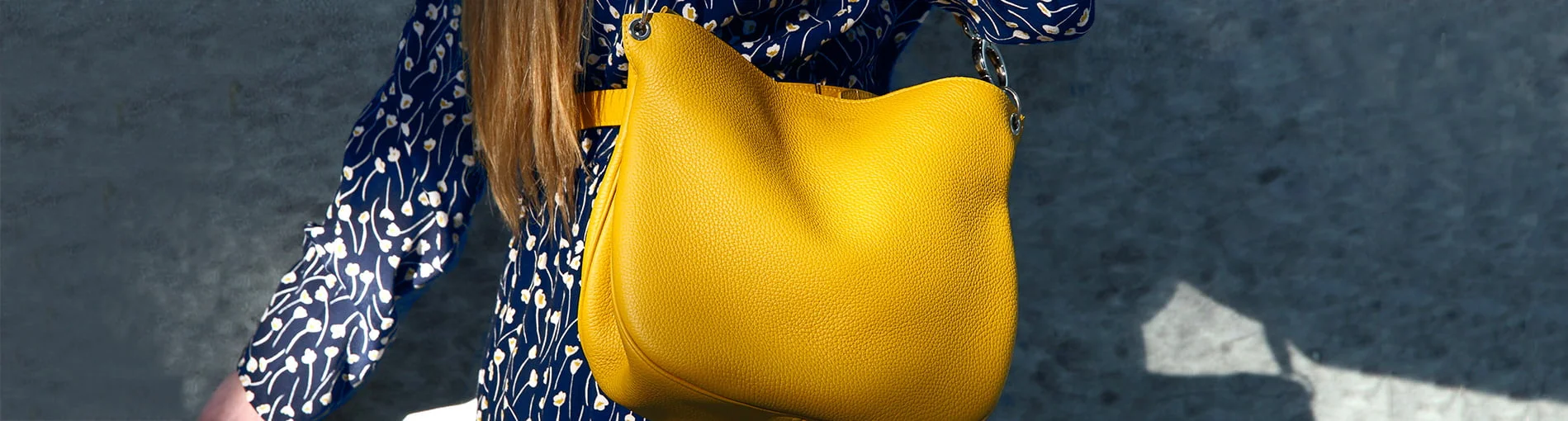 Une personne portant une tenue à motifs bleu et blanc tient un sac à main artisanal, mettant en valeur une fabrication française exceptionnelle avec sa finition en cuir jaune saisissante.