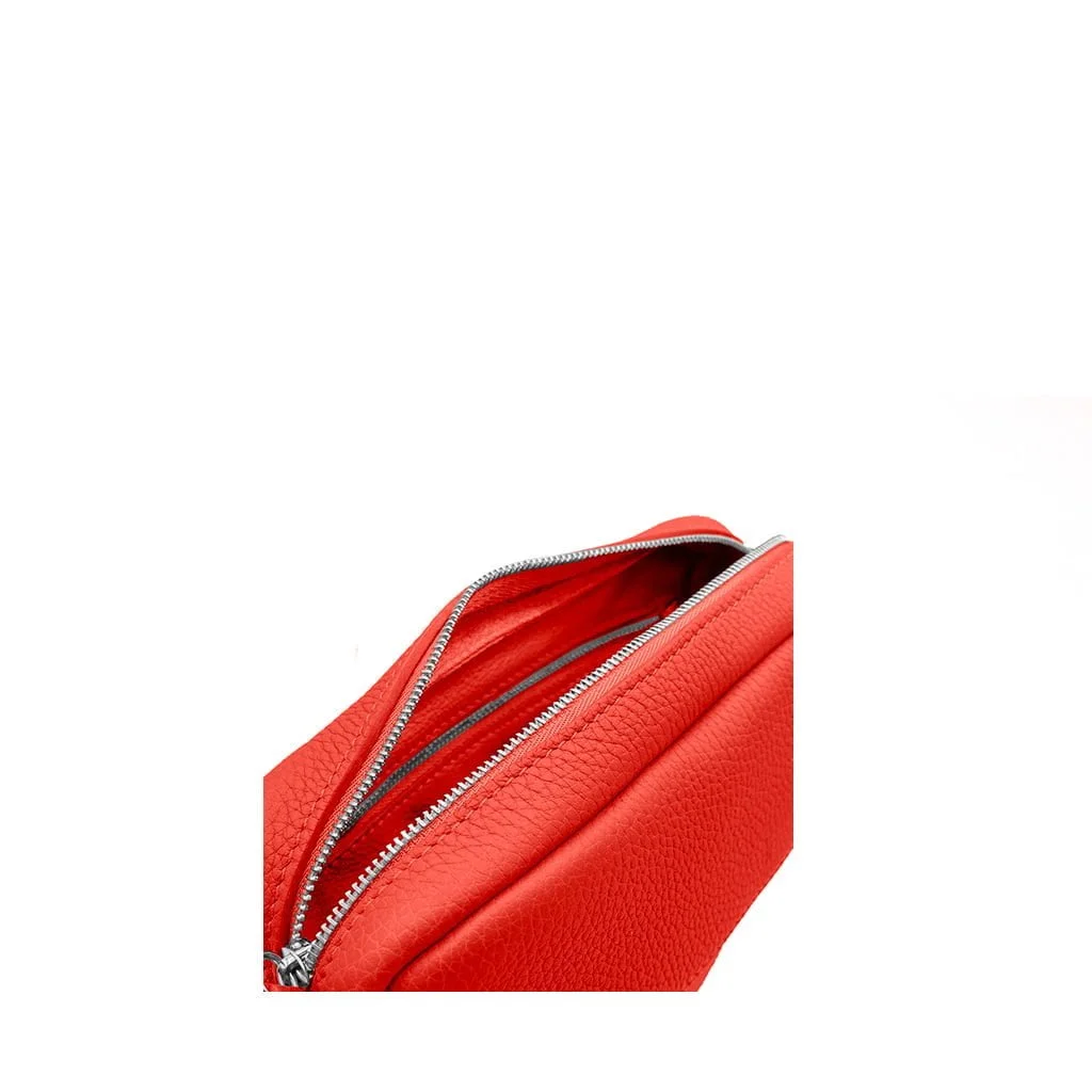 Gros plan d'un sac en cuir orange avec une fermeture éclair argentée partiellement ouverte sur fond blanc.