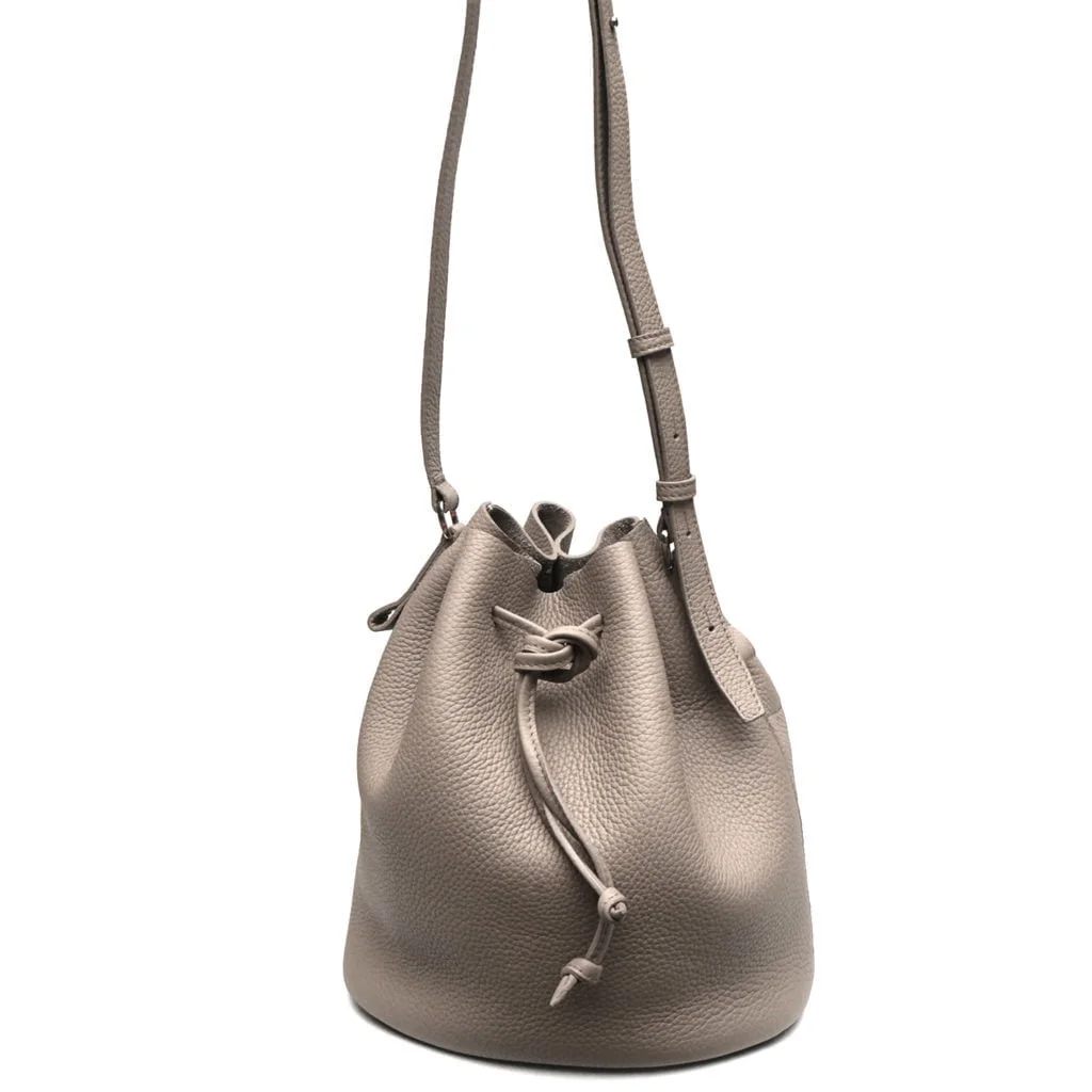 Sac seau en cuir gris avec cordon de serrage et bandoulière réglable.