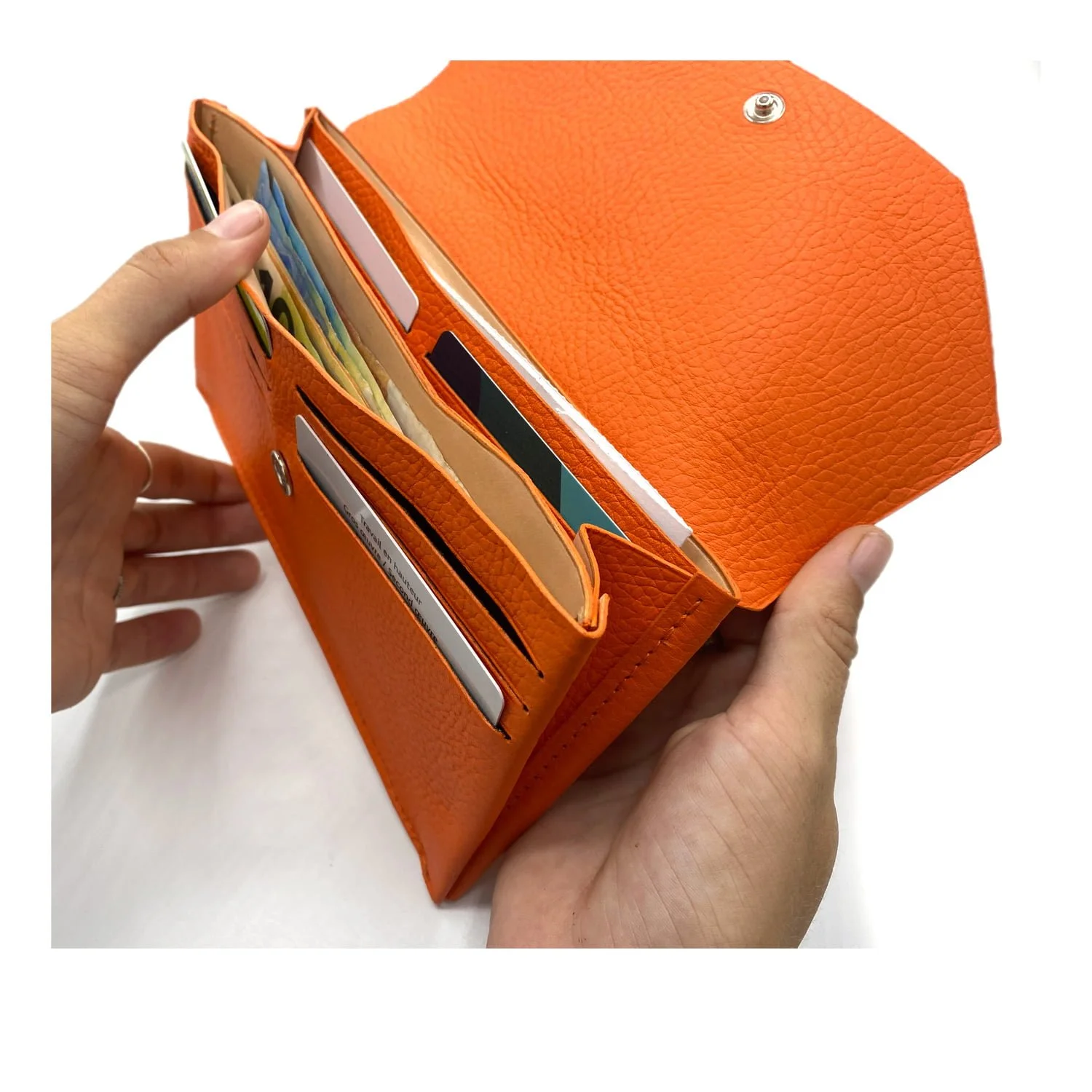 Mains tenant un portefeuille orange ouvert montrant de l'argent et des cartes à l'intérieur.