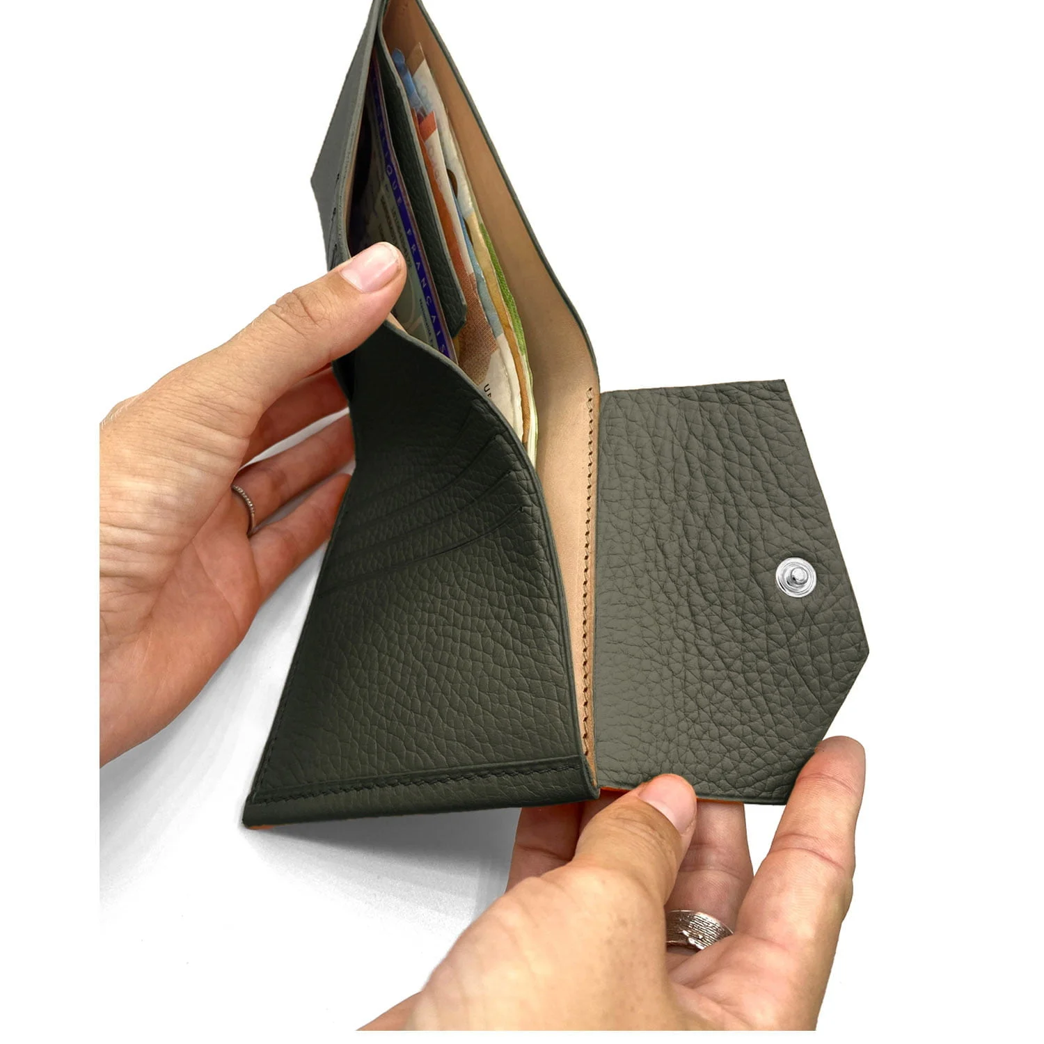 Mains ouvrant un portefeuille en cuir vert foncé, révélant de l'argent et des cartes.
