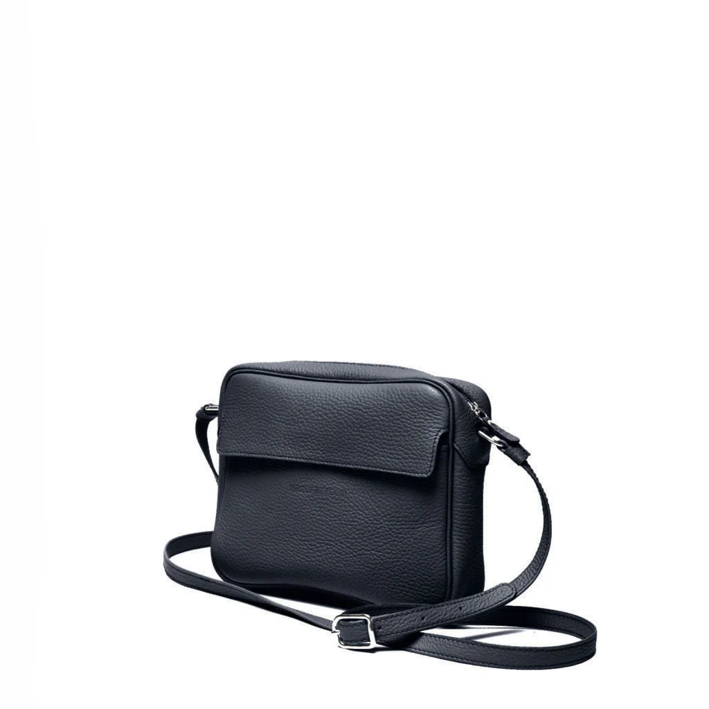 Un sac à bandoulière en cuir noir avec un rabat avant et une bandoulière réglable est positionné sur un fond blanc.