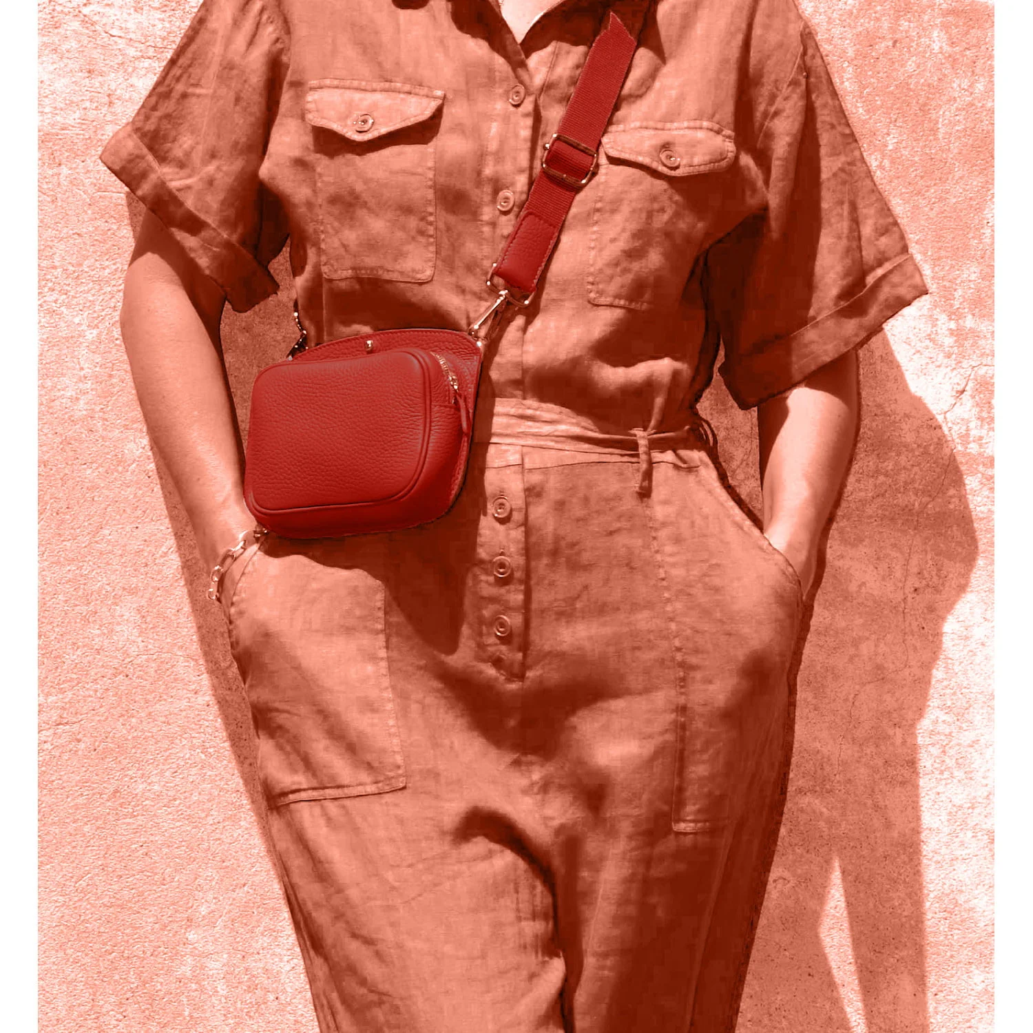 Personne portant une combinaison boutonnée avec les mains dans les poches, portant un sac à bandoulière rouge.