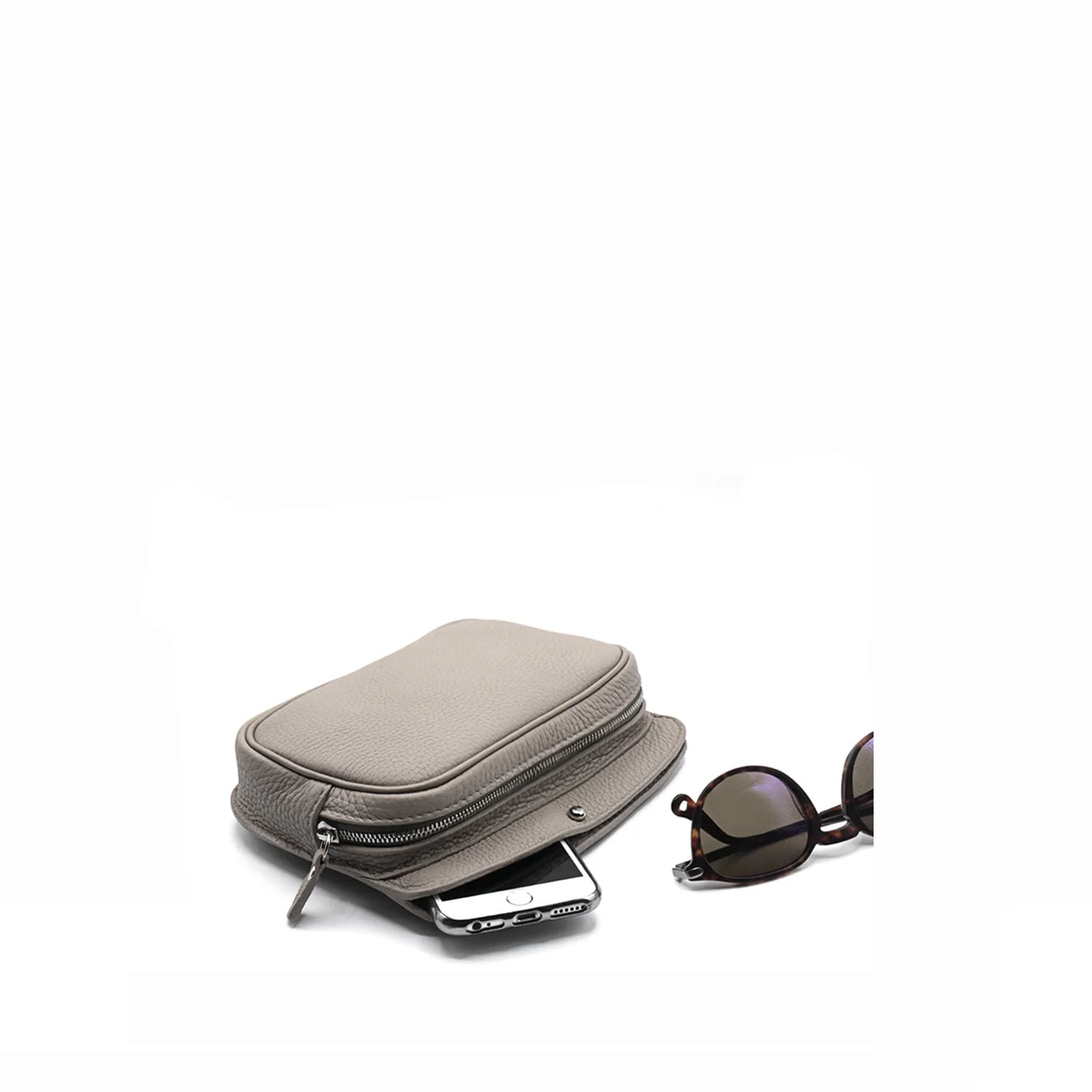 Une pochette zippée beige avec un smartphone partiellement à l'intérieur se trouve à côté de lunettes de soleil rondes avec des verres foncés sur une surface blanche.