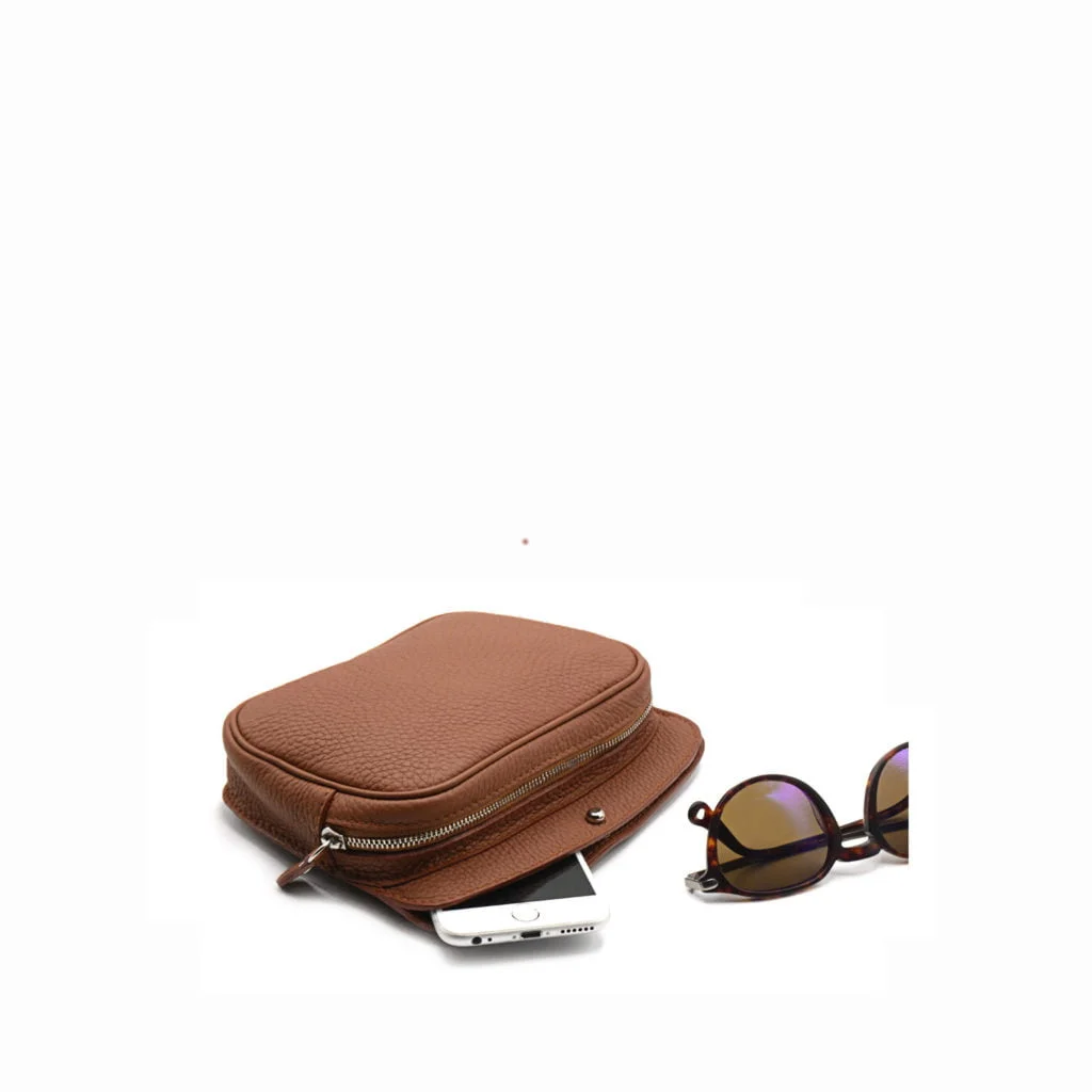Une pochette en cuir marron avec fermeture éclair, partiellement ouverte pour révéler un smartphone. Des lunettes de soleil aux verres foncés sont placées à côté de la pochette.