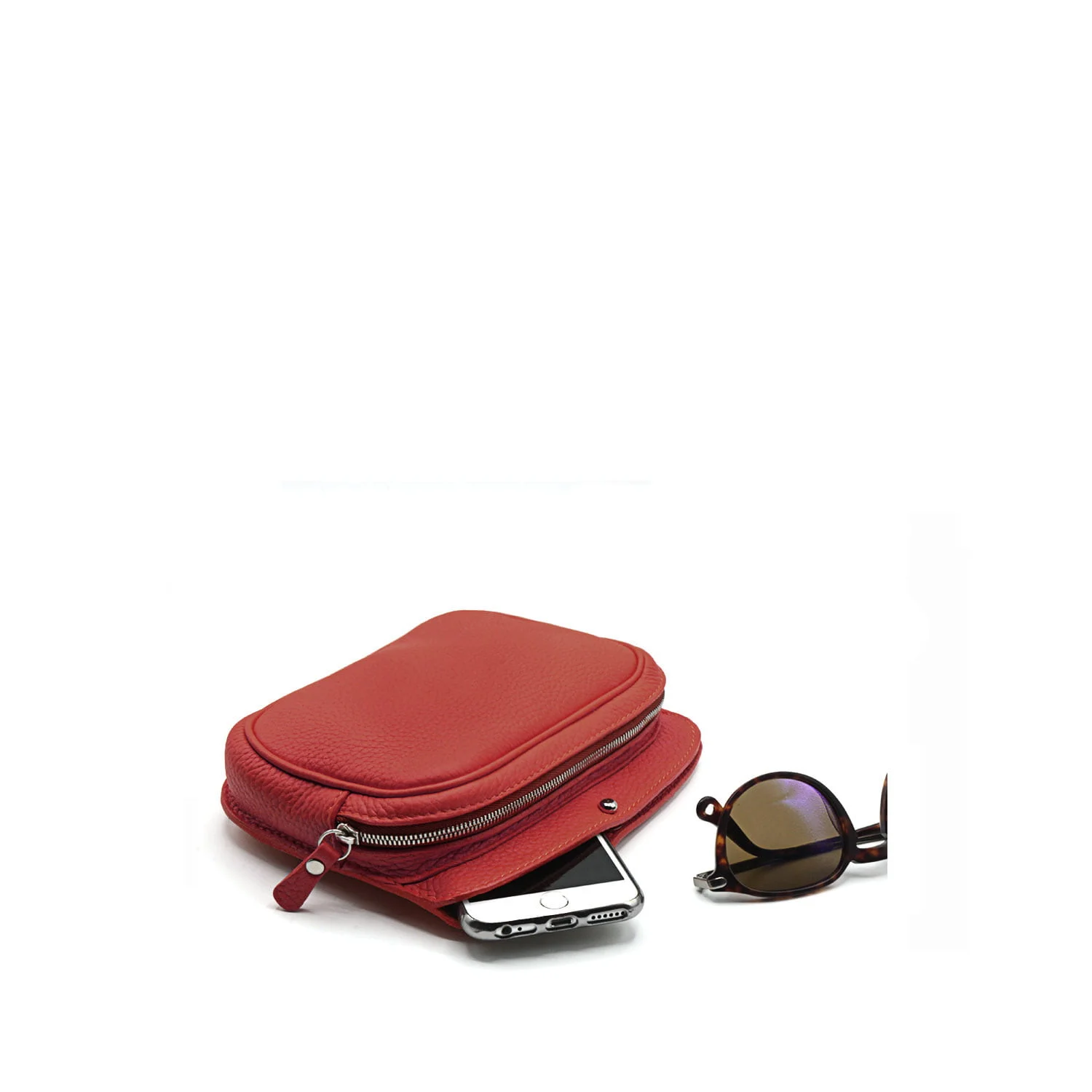 Un sac à main en cuir rouge avec un smartphone et des lunettes de soleil à côté sur un fond blanc.