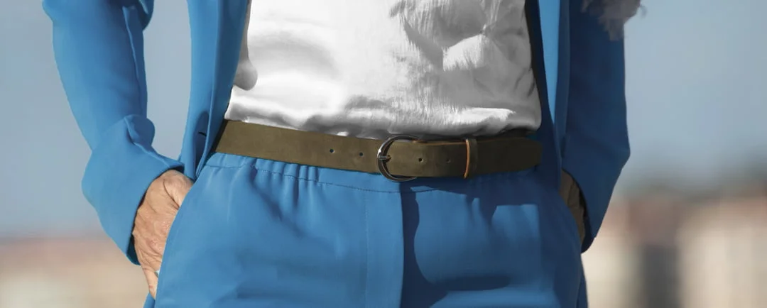 Personne en costume bleu avec les mains dans les poches, portant une chemise blanche et une ceinture foncée.