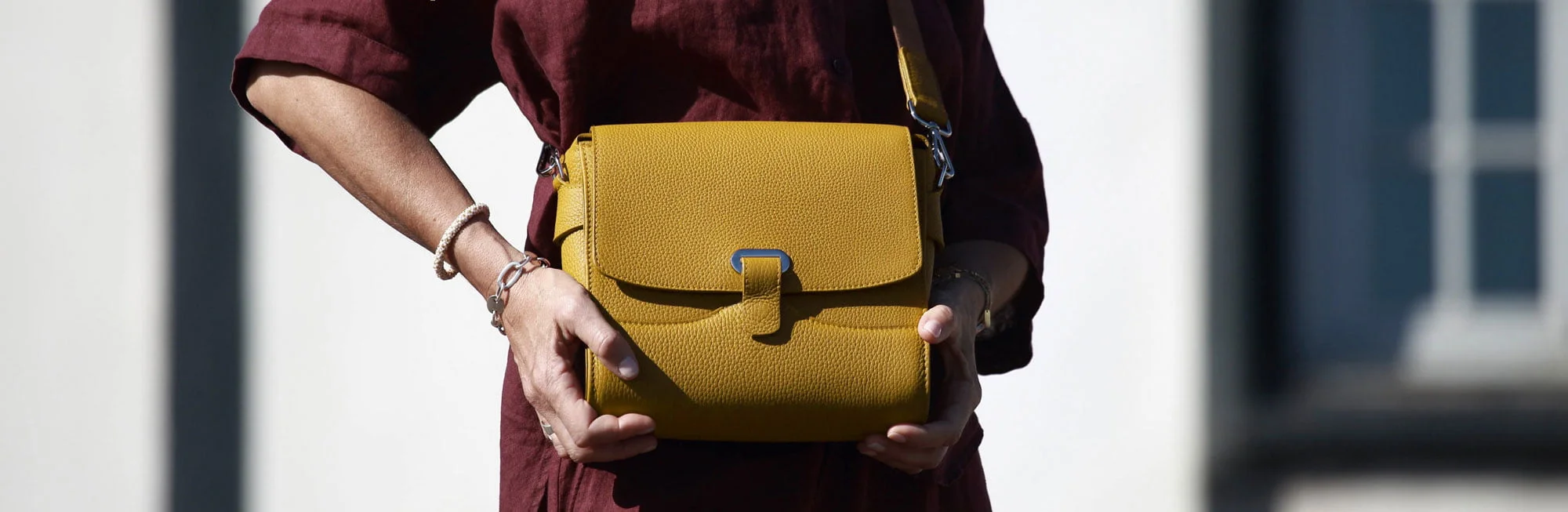 Une personne vêtue d'une robe marron tient un sac à main artisanal jaune moutarde, doté d'un fermoir en argent, mettant en valeur une fabrication française exquise.