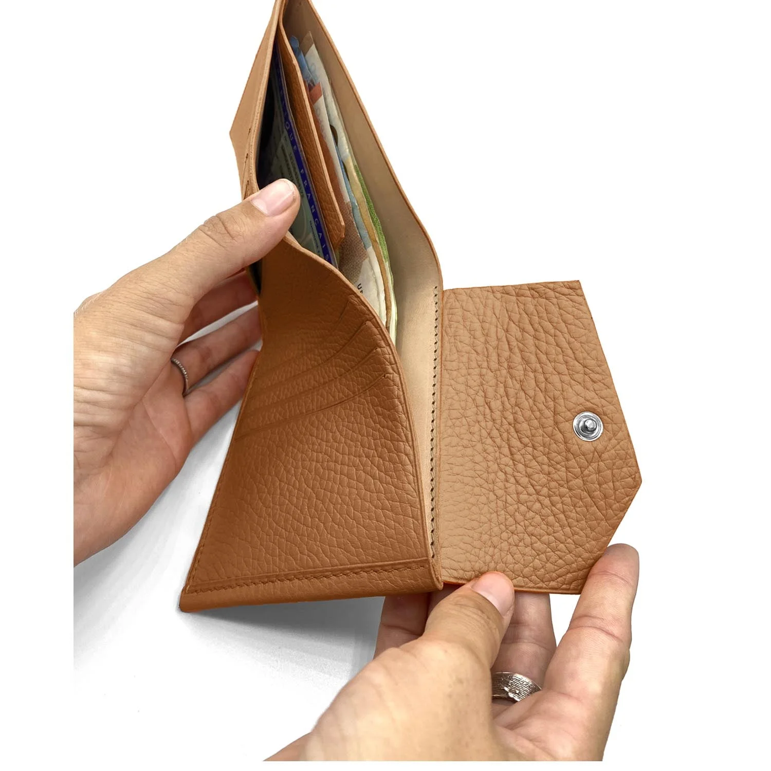 Mains tenant un portefeuille en cuir beige ouvert, révélant plusieurs emplacements pour cartes et une section avec du papier-monnaie.