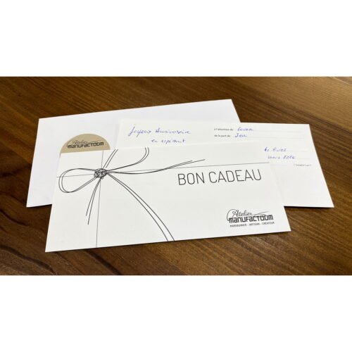 Carte-cadeau étiquetée BON CADEAU sur une table, avec une enveloppe contenant un texte manuscrit en arrière-plan.