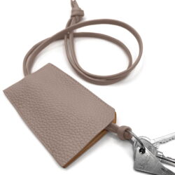 Une pochette à clés en cuir beige texturé avec un cordon et des clés attachées sur fond blanc.
