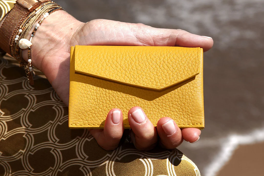 Main tenant un petit portefeuille jaune texturé de style enveloppe avec un fond à motifs géométriques.