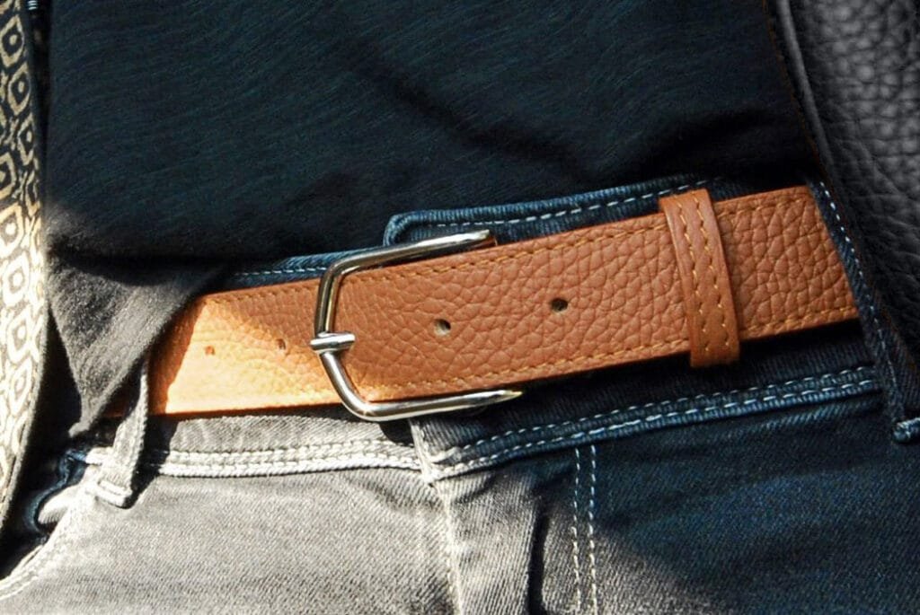 Gros plan d'une ceinture en cuir beige attachée autour d'une personne portant un jean foncé et une chemise noire.