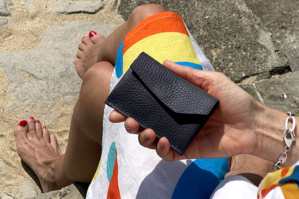 Une personne vêtue d'une robe à rayures colorées tient un portefeuille en cuir texturé noir, assise pieds nus sur des marches en pierre.