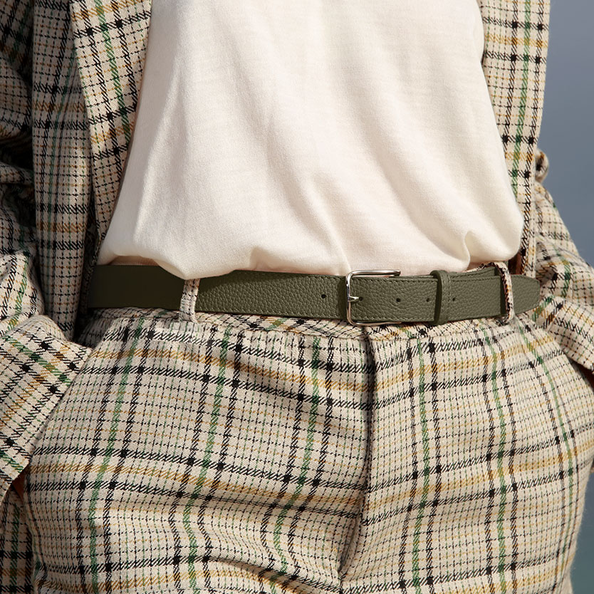 Une personne portant un blazer et un pantalon à carreaux par-dessus une chemise blanche, rehaussés d'une ceinture vert sauge.